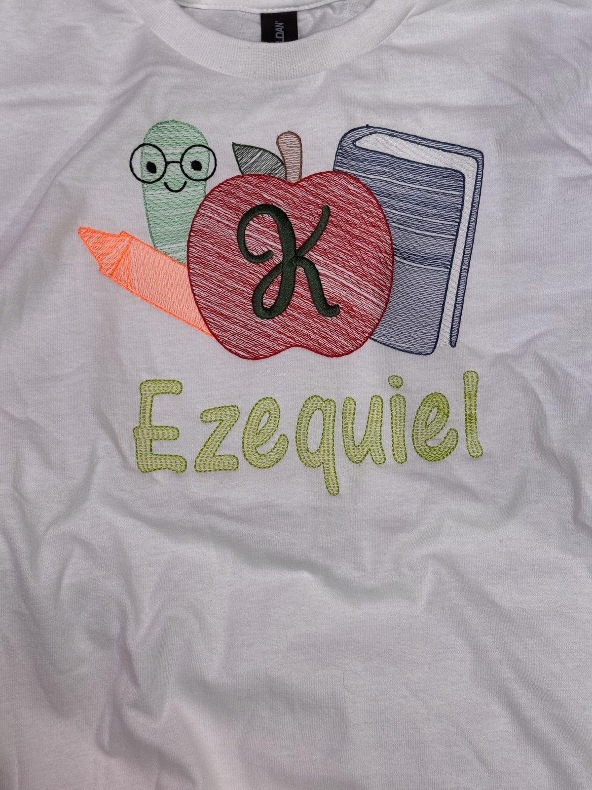 White children’s shirt personalized for Ezequiel with apple pencil and book embroidery