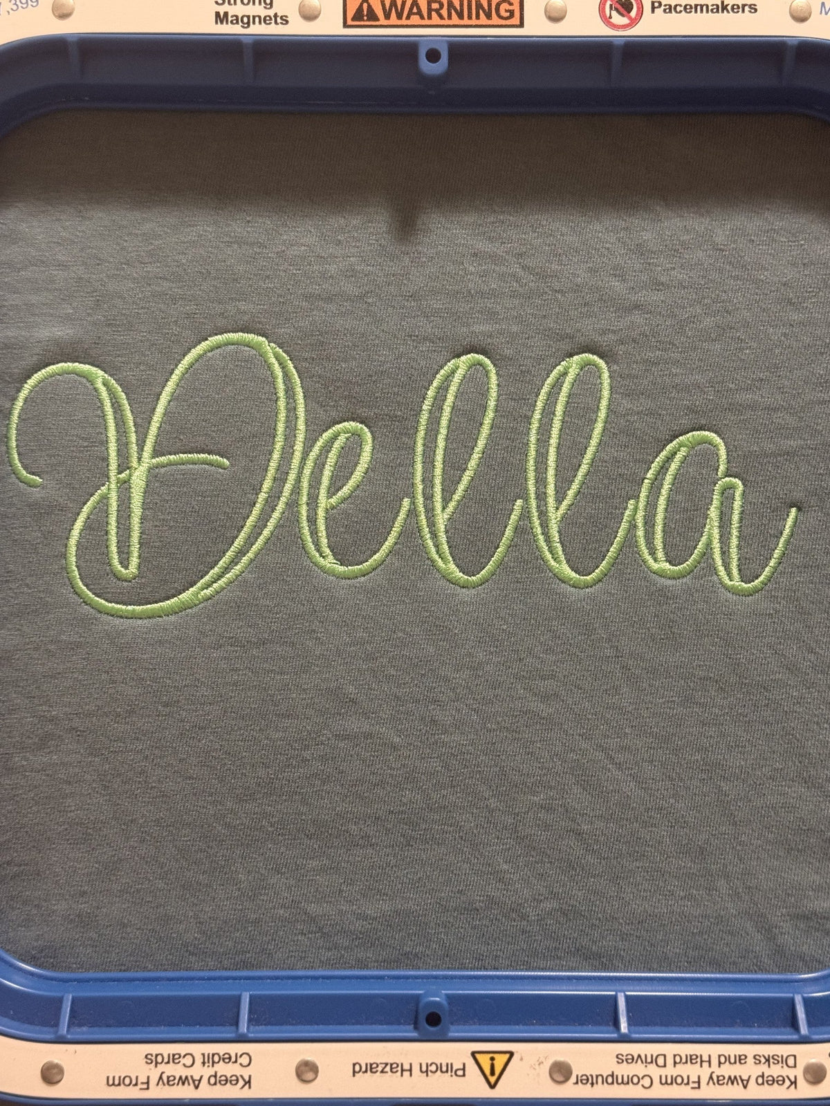 Gray fabric embroidered with the script name Della in green thread
