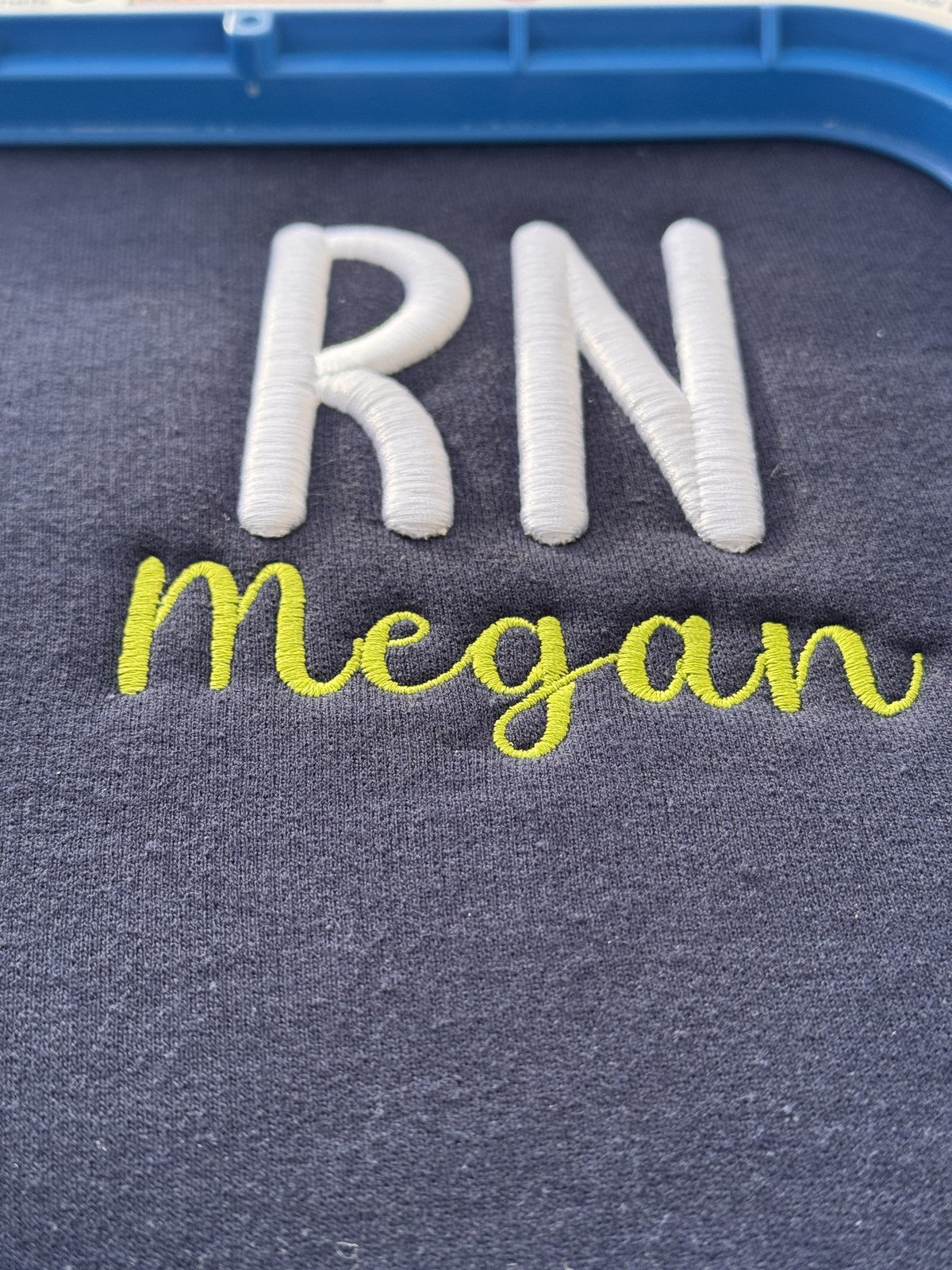 Dark fabric embroidered with RN and the name Megan in bright thread colors