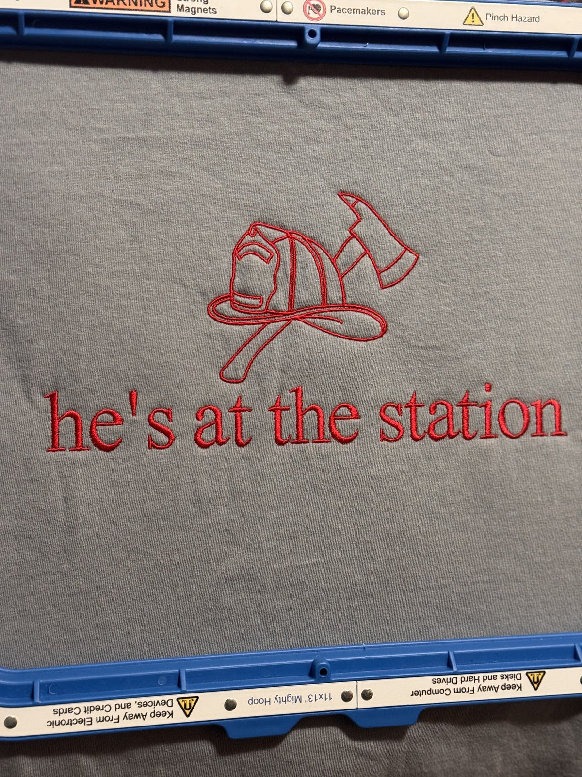 Gray fabric with firefighter helmet embroidery and He’s At The Station text