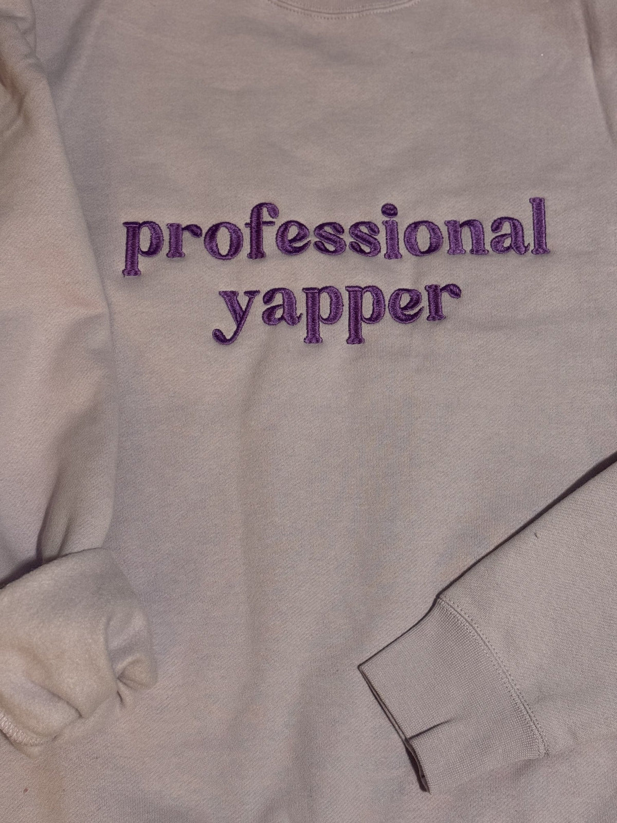 Gray sweatshirt embroidered with Professional Yapper in purple lettering