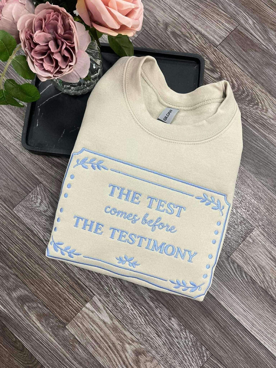 Cream embroidered faith sweatshirt reading The Test Comes Before The Testimony