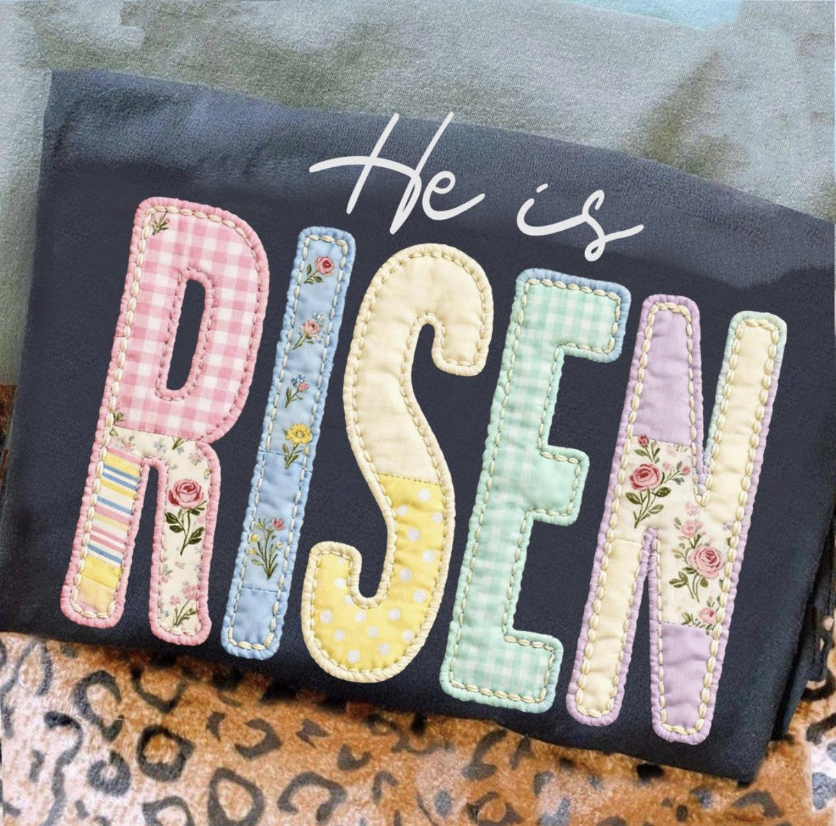 Dark shirt with He Is Risen faith applique in pastel patterned lettering