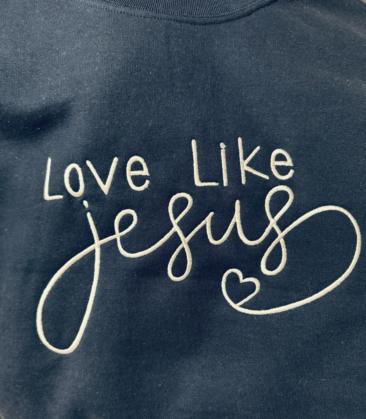 Dark sweatshirt embroidered with the phrase Love Like Jesus and a heart