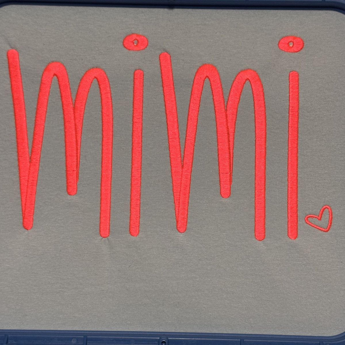 Gray fabric embroidered with red mimi lettering and a small heart
