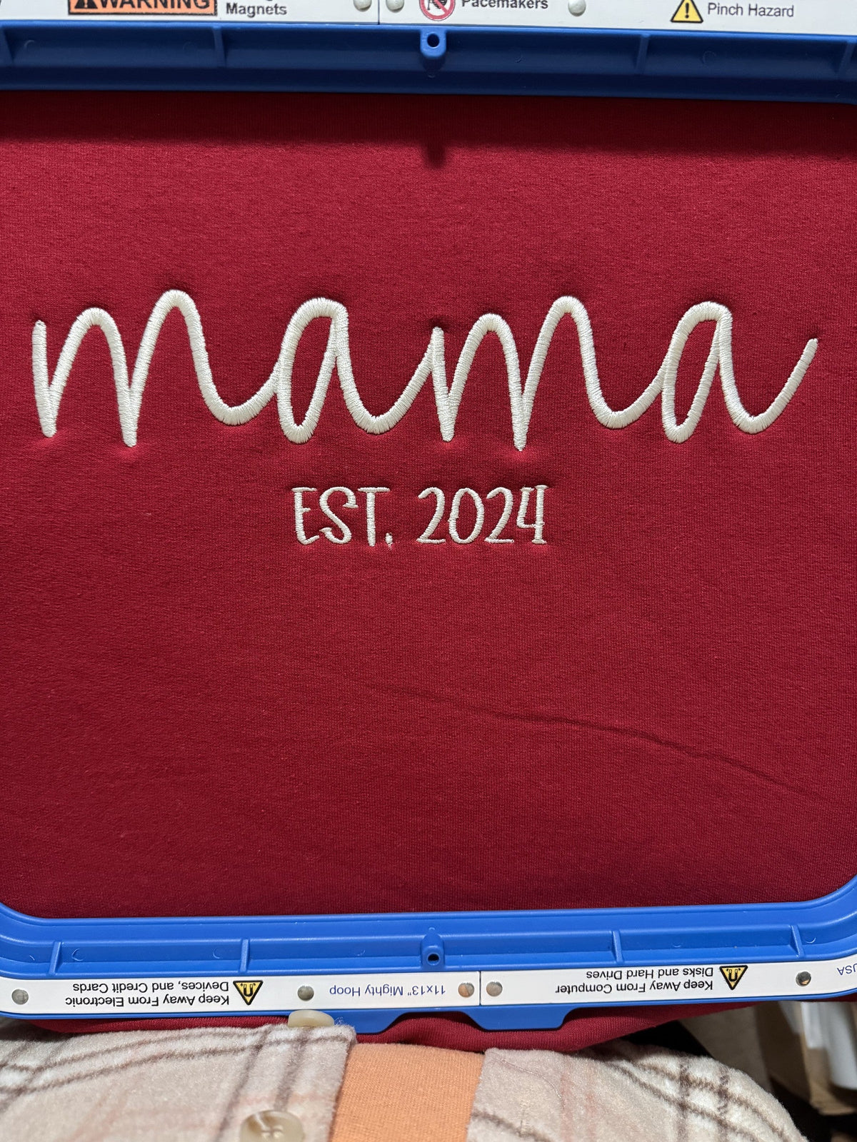 Red fabric embroidered with MAMA and established-year lettering in an embroidery hoop