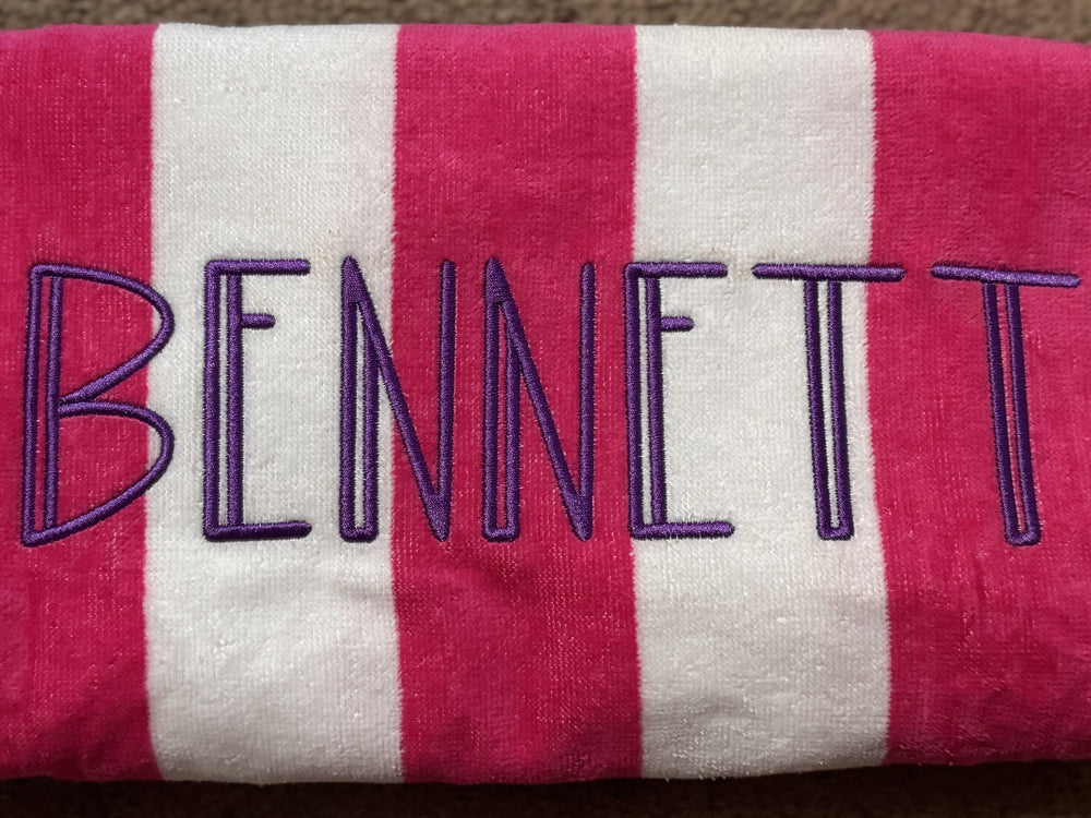 Pink and white striped towel personalized with the name Bennett in navy embroidery